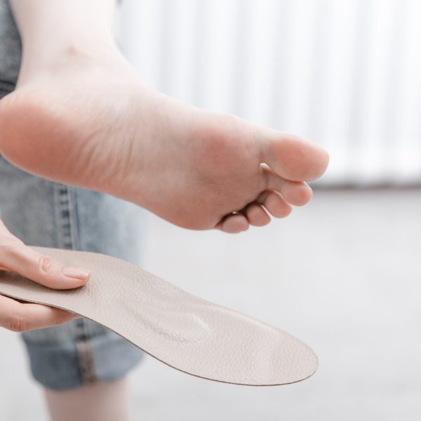 Woman fitting orthopedic insole indoors, close up. Girl holding an insole next to foot at home. Orthopedic insoles. Foot care banner. Flat Feet Correction. Treatment and prevention of foot diseases Woman fitting orthopedic insole indoors, close up. Girl holding an insole next to foot at home. Orthopedic insoles. Foot care banner. Flat Feet Correction. Treatment and prevention of foot diseases.